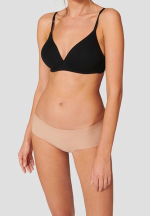 Weiblicher Oberkörper trägt einen schwarzen BH mit dünnen Trägern und nahtlose, hautfarbene Hipster-Slips vor einem hellgrauen Hintergrund.