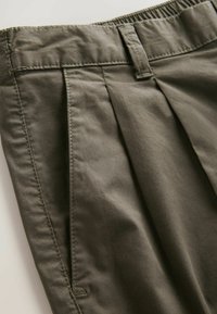 Olivengrønne bukser med plisseret frontdesign, elastisk talje og glat stoftekstur. Har pænt syede sømme og lommer.