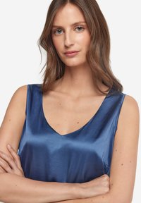 Satin topp i djupblått, med V-ringning och ärmlös design. Slät yta och lätt lyster med minimalistiska stil detaljer.