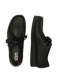 Musta nahkakengät, joissa on tekstuuripinta, nauhakiinnitys, paksu kumipohja ja Clarks-logo näkyvästi esillä pohjallissa.