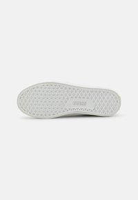 White sneaker outsole with a textured, patterned surface. Features a triangular grip pattern and a raised "GUESS" logo.