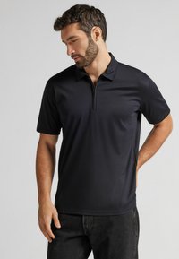 Polo negro de manga corta con cuello con cremallera, hecho de una tela suave, con un ajuste relajado y un diseño minimalista.