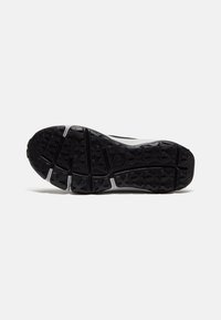 Semelle de chaussure de sport noire avec un revêtement en caoutchouc texturé et des accents blancs. Possède un motif multi-directionnel pour une adhérence et une stabilité optimales.
