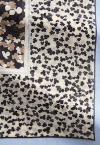 Jedwabny szalik z kwiatowym wzorem w czerni, beżu i bieli na jasnym tle, z ozdobnym kątowym wzorem i miękką teksturą.