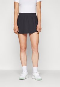Black athletic skirt with a flared design, elastic waistband, and smooth fabric. Worn with white sneakers and ankle-length socks.
