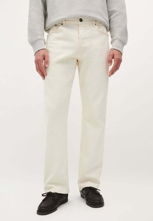 Jeans in denim beige chiaro con taglio dritto, dotati di tasche, chiusura con bottone e dettagli di cucitura discreti. Indossati con scarpe nere.