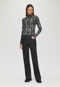 Haut à manches longues avec un motif de peau de serpent noir et argent, associé à un jean noir taille haute et des bottes noires chunky.