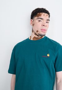 Teal cotton t-shirt featuring a round neckline and short sleeves, with a small embroidered Carhartt logo in yellow and red.