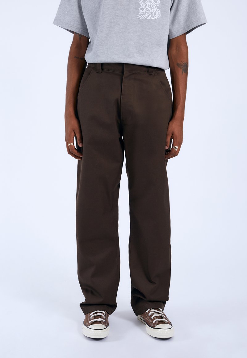 Braune, locker sitzende Hosen aus Baumwolle mit hoher Taille und Seiten- taschen, kombiniert mit braunen und weißen Sneakers.