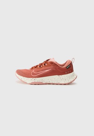 Koraalroze Nike hardloopschoen met gevlekte witte zool, vetersluiting en Gore-Tex-label op de hiel, zijaanzicht op een effen achtergrond.