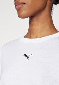 Bílá bavlněná tričko s černě vyšitým logem Puma na levé části hrudi. Kolačný výstřih se hladkým povrchem.