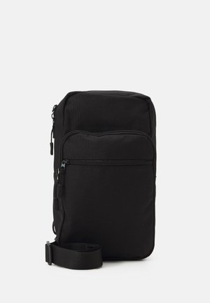 Black nylon crossbody bag with a zippered front pocket, adjustable strap, and a smooth texture. Compact rectangular shape.