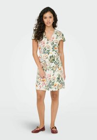 Vestido envolvente floral con mangas cortas, con un fondo crema decorado con hojas verdes y flores de colores. Tela ligera, corte a la altura de la rodilla.