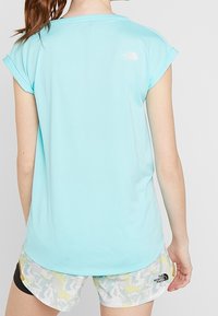 T-shirt de sport à manches courtes bleu clair avec une coupe ample, orné d'un petit logo blanc au dos. Associé à un short à motifs.