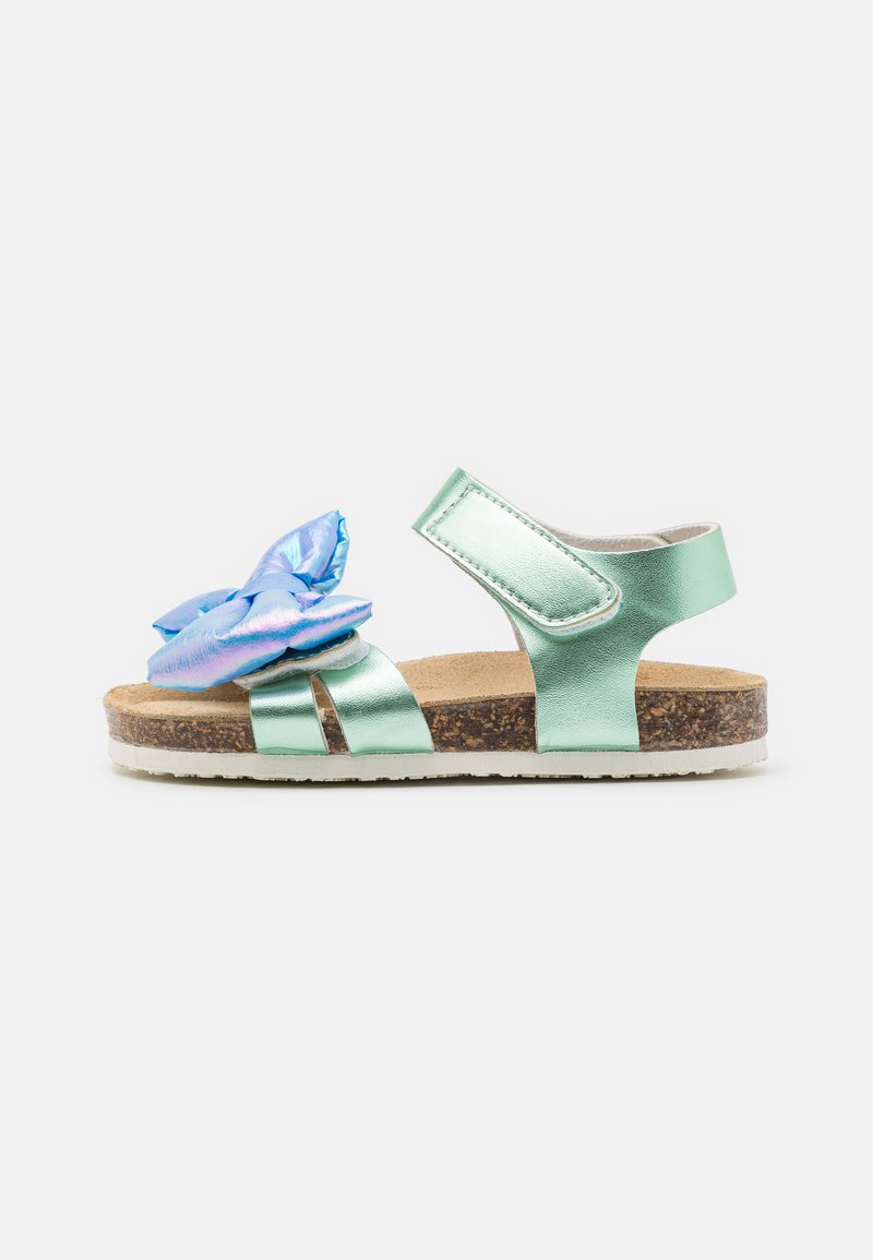 Gröna metalliska sandaler med en stor blå syntetisk blomma som accent, korkfotbädd, justerbar rem och vit gummisula.