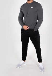 Sudadera gris de manga larga con cuello redondo y pequeño logotipo, combinada con pantalones cargo negros con bolsillos laterales y zapatillas blancas con detalles de malla.
