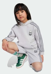 Ljusgrå huvtröja med grå ränder och logotyp, matchad med shorts i samma färg. Gröna sneakers med vita ränder och grå strumpor med gröna accenter.