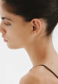 Aro de oreja de oro con un diseño de concha texturizada, que presenta una forma curva y elegante. La superficie lisa y el brillo sutil realzan sus detalles.