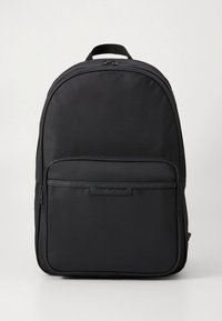 Μαύρο σακίδιο από νάιλον με λεία υφή, καμπύλο σχήμα και εμπρόσθια τσέπη με φερμουάρ. Διαθέτει πάνω χερούλι και λογότυπο στο μπροστινό πάνελ.