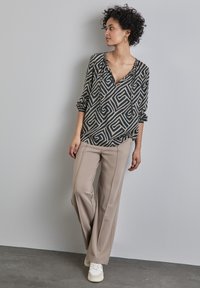 Blusa a maniche lunghe con motivo geometrico bianco e nero. Pantaloni beige a gamba larga. Sneakers bianche con suola testurizzata completano l'outfit.
