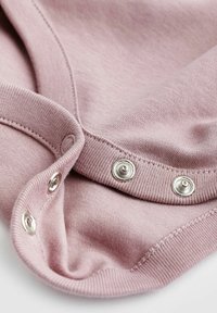 Šviesiai rožinė medvilnė su lygiu paviršiumi, puošta sidabriniais spaudžiamais mygtukais ir grublėtomis kraštinėmis prie apykaklės ir juosmens.