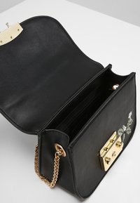 Černá kožená crossbody taška se zlatým řetízkem, zlatým uzávěrem, květinovou výšivkou na přední straně a vnitřním oddílem se sloty na karty.