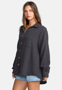 Donkergrijs overhemd met kraag, grote knopen, een borstzak en lange mouwen, gemaakt van textuurstof. Gepaard met denim short.