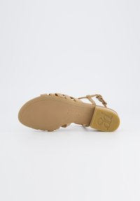 Brązowe sandały na płaskiej podeszwie z cienkimi paskami, z teksturowaną wkładką i tłoczonym logo na pięcie. Regulowany pasek przy kostce zapewniający odpowiednie dopasowanie.