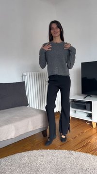 Pelēks adīts kardigāns ar apaļu izgriezumu un pogu aizsegu, papildināts ar melnām platiem biksēm ar sānu šķēlumiem. Melnas slip-on kurpes.