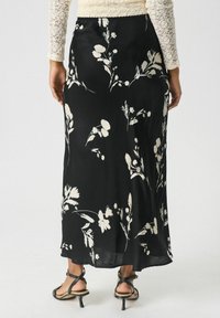 Jupe noire à motifs floraux, fabriquée en tissu doux, avec des motifs floraux blancs. De longueur inférieure à la cheville, elle présente une silhouette fluide et un subtil éclat.