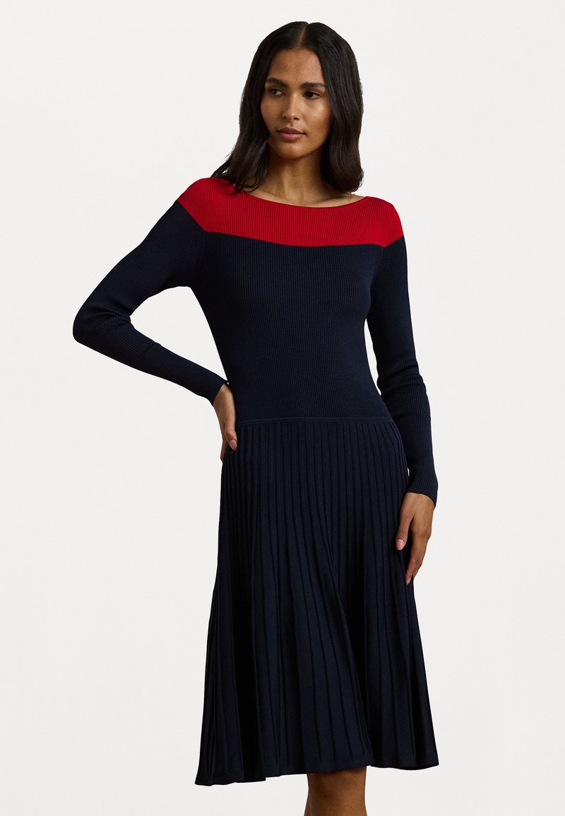 Vestido de malha com um top canelado vermelho e uma saia plissada azul-marinho. Mangas longas e um decote barco completam o design. Tecido macio e elástico.