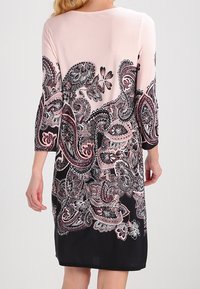 De shift dress heeft een lichtroze bovenkant en een zwarte rok, versierd met ingewikkelde paisley- en bloempatronen in tinten van roze en wit.