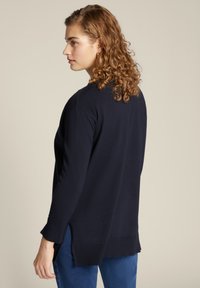 Maglione blu navy con maniche lunghe e spacchi laterali, realizzato in tessuto morbido, con collo rotondo e polsini a costine.