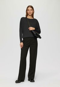 Schwarzes Langarmtop mit verstreuten Verzierungen, kombiniert mit weiten schwarzen Hosen und klobigen schwarzen Schuhen sowie einer schwarzen Schultertasche.