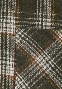 Tessuto plaid verde e bianco con accenti rossi e gialli, caratterizzato da una texture in lana e linee incrociate di varie larghezze.
