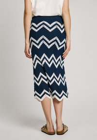 Knälång marinblå kjol med ett vitt zigzag-mönster, tillverkad av texturerad stickad tyg med en scalloped fåll.