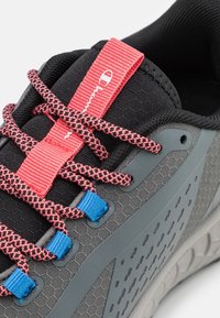 Scarpa sportiva grigia con una tomaia testurizzata, lacci rosa e blu, e un motivo esagonale sul lato. Presenta una suola imbottita.