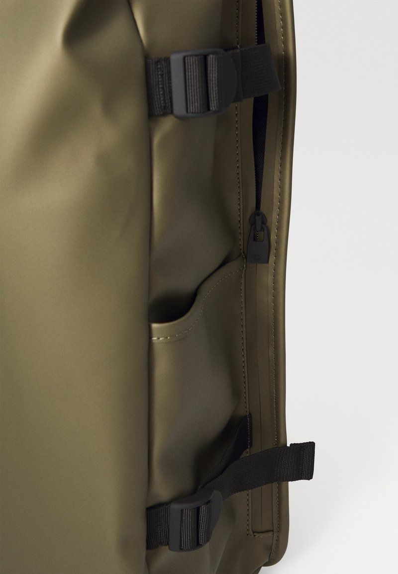 Sac à dos imperméable vert avec une texture lisse, plusieurs compartiments, des bretelles noires et une fermeture éclair au design minimaliste.