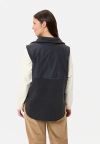 Ärmellose Weste aus dunkelgrauem Stoff mit einem unteren Abschnitt aus Fleece. Sie verfügt über einen Kragen und ein glattes Obermaterial sowie einen abgerundeten Saum.