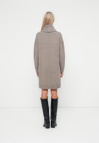 Vestido de malha bege com gola alta, mangas longas e bainha canelada. Combinado com botas pretas até ao joelho. Textura suave.