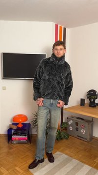 Casaco de pelo sintético cinza com gola alta, combinado com umas calças de ganga azul claro e sapatos castanhos escuros. Design sólido, sem padrões ou detalhes visíveis.