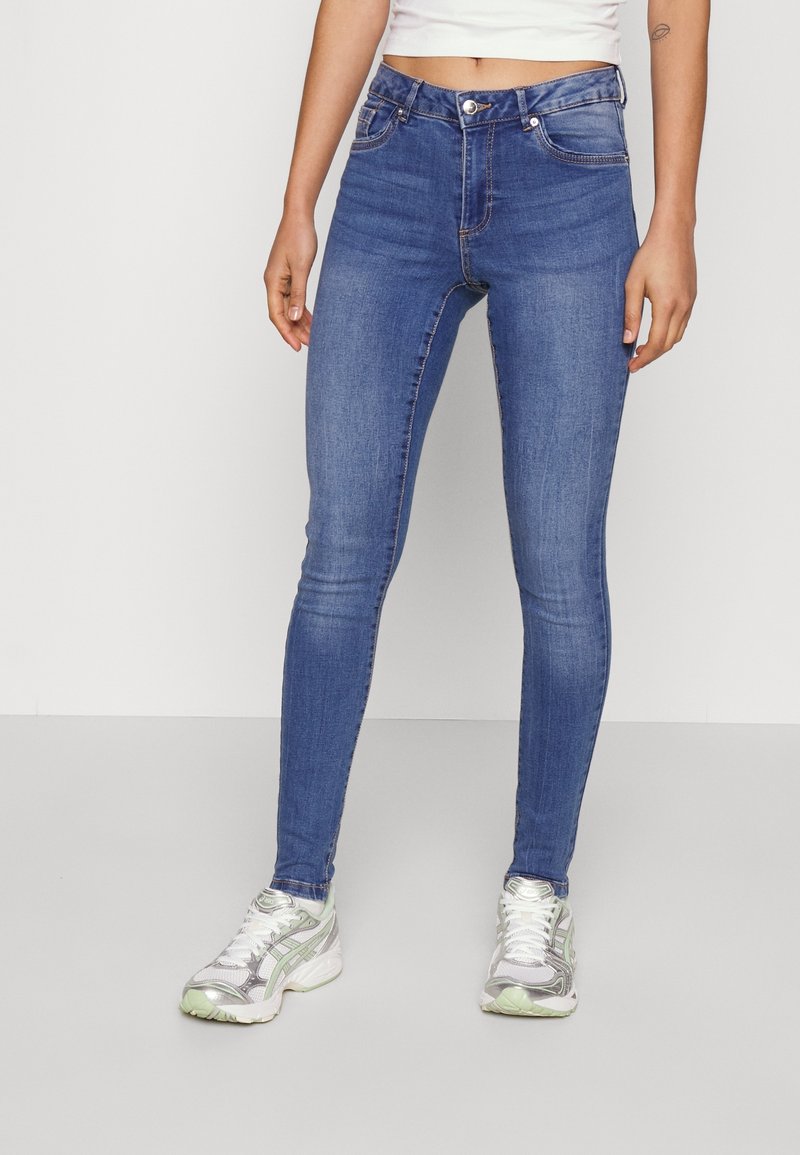 Jean skinny bleu en denim, avec une taille haute, des poches frontales et des détails de couture subtils, associés à des baskets argentées.