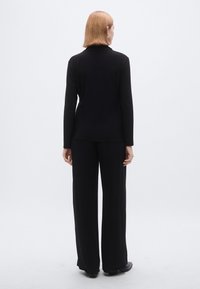 Zwart lang mouwen top en loszittende broek, gladde stof, minimalistisch ontwerp, geen zichtbare patronen of hardware, model gezien van achteren.