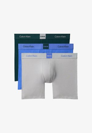 Trzy pary bokserek Calvin Klein w kolorach szarym, niebieskim i ciemnozielonym, ułożone jedna na drugiej, z widocznymi paskami z logo marki.