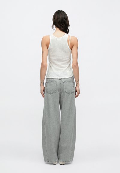 Άσπρο ριμπ τοπ με λεπτές τιράντες, σε συνδυασμό με ανοιχτογριζά τζιν παντελόνια με φαρδύ πόδι, πίσω τσέπες και άνετη εφαρμογή.