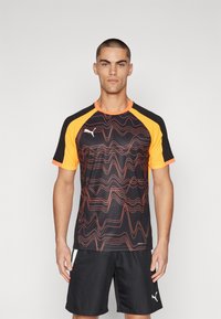 Kortærmet atletisk skjorte i sort med orange detaljer og bølgede røde mønstre, lavet af let og åndbart stof. Har en rund halsudskæring.