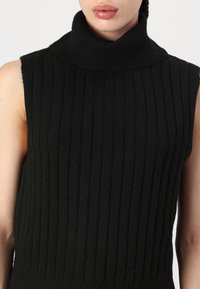 Svart ribbadärmlös polotröja med en strukturerad stickning, med hög krage och åtsittande design. Slätt tyg, minimal detaljering.