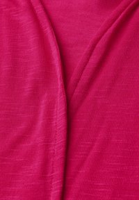 Tissu stretch fuchsia avec une texture lisse, présentant un design à col en V et de subtils détails tissés. Idéal pour le superposition.