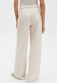 Beige wijde broek met elastische tailleband en achterzak, gemaakt van een glad, zacht materiaal met strakke, rechte lijnen.