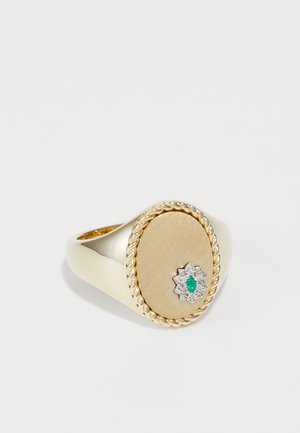 Gold ring featuring a smooth, oval top with a twisted rope edge and a star-shaped design with a central emerald and surrounding crystals.